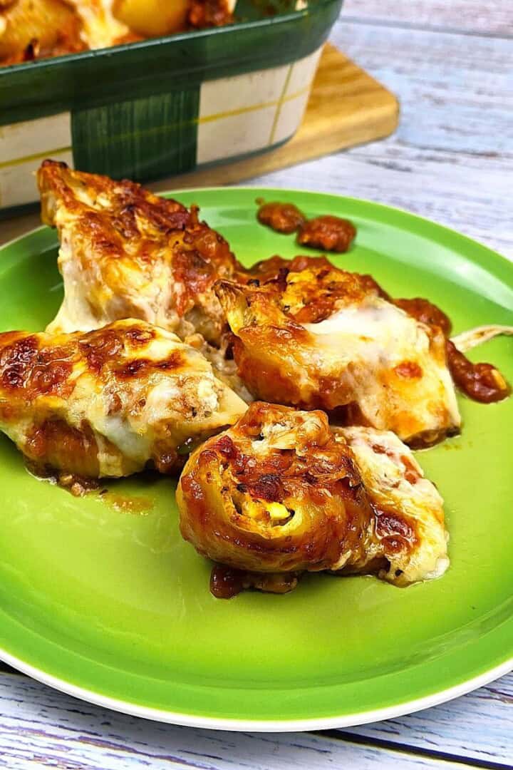 Four cheesy chicken stuffed shells served on a green plate with rich tomato sauce.