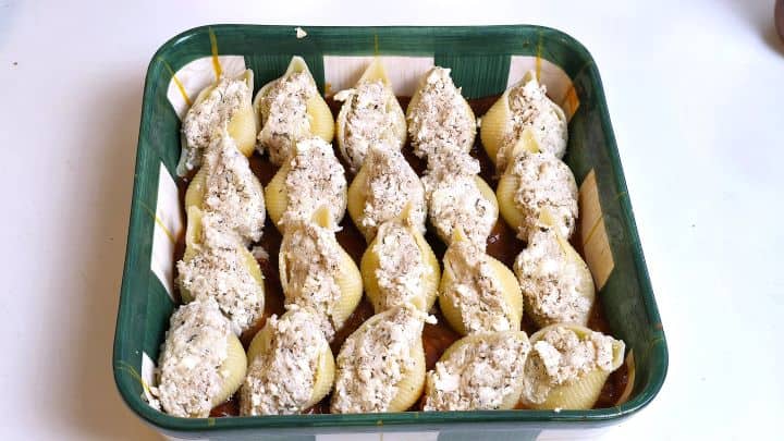 Spoon filling jumbo pasta shells with cheesy chicken mixture in a baking dish over tomato sauce.