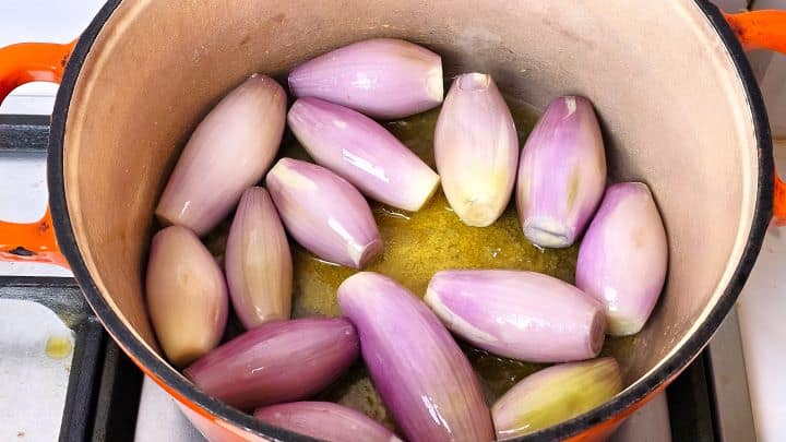 Whole peeled shallots cooking in olive oil in a cast iron Dutch oven.