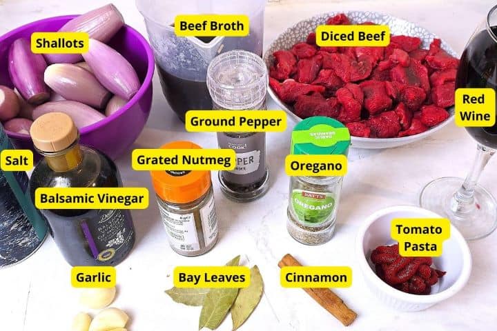 Ingredients for Greek beef stifado including diced beef, whole peeled shallots, red wine, garlic, cinnamon stick, and spices.