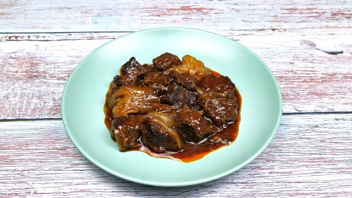 A hearty portion of Greek beef stifado with tender beef and whole sweet shallots served on a green plate.