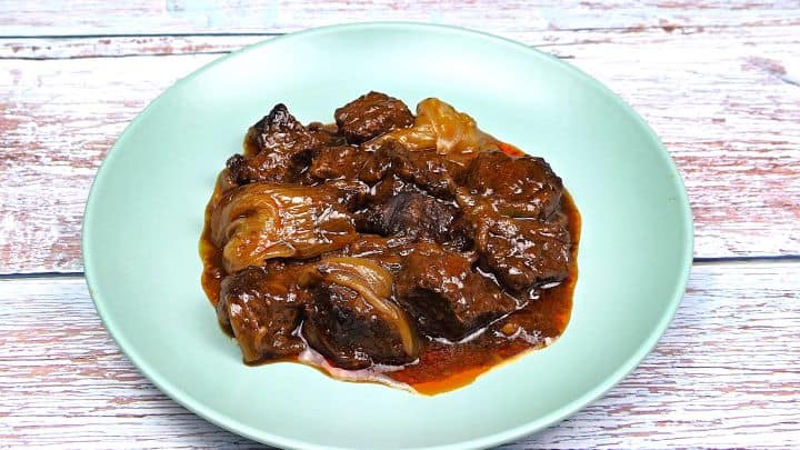 Close-up of melt-in-the-mouth Greek beef stifado on a green plate garnished with fresh parsley and served with crusty bread.