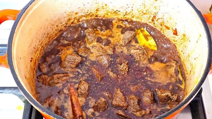 Pouring dry red wine and balsamic vinegar into the Dutch oven to deglaze the seared beef and spices.